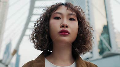 Close Up of Beautiful Young Curly-Haired Asian Woman Standing Outdoors and Looking at the Camera.