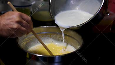 Female hands add milk to bowl of beaten eggs with mixer. Waffle cookie recipe step by step. Hand mixer beats eggs, milk