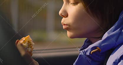 Close-up footage of a teenager girl eating burger while sitting in a car.