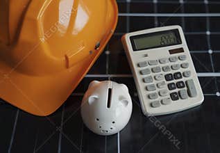 Construction worker hardhat piggy bank and calculator resting on solar panels