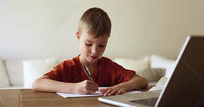 Cute little boy makes assignment sit at table with laptop