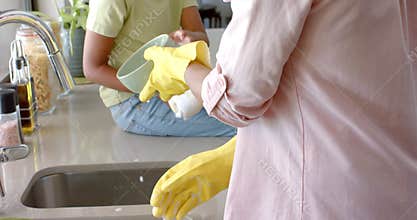 Biracial mother and daughter washing and drying dishes in kitchen, slow motion