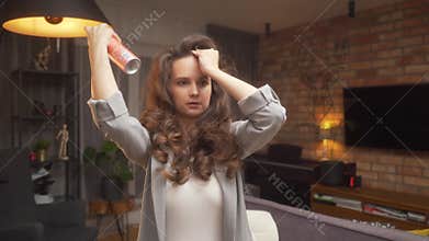 A woman fixes bangs and voluminous curls with hairspray, styling hair at home.