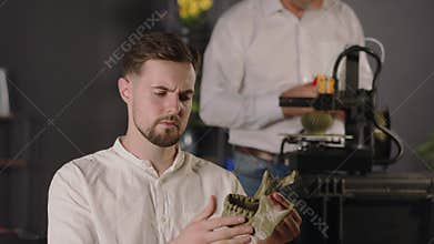 A young guy research assistant holds in hands and views khaki coloured plastic model of human mandible. A middle aged