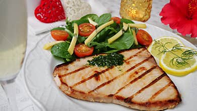 Grilled swordfish steak with fresh salad, tomatoes and cheese on a plate rotating. Valentines day. Pour champagne into a glass.