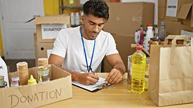 Handsome hispanic man volunteering in warehouse, organizing donations, writing inventory list