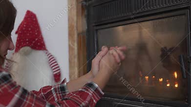 Beautiful woman warming her hands by the fireplace.