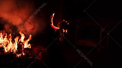 the silhouette of a woman looking at her jewelry with a face full of sadness and the fire burning around her