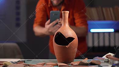 Bearded male archaeologist working late at night photographing an old vase as an archaeological artifact in his office