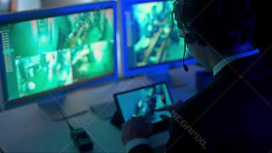Man security guard officer working on pc in monitoring center, watching video from cameras, back shot. Computers and big