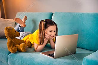 Photo portrait of adorable small girl lying sofa netbook watch cartoon dressed stylish yellow garment preschoolers