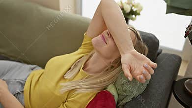 Cheerful young blonde woman having fun at home, confidently covering eyes with arm, wearing a t-shirt â€“ the joy of a funny