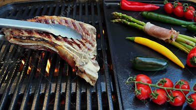 Beef T-Bone steak grill turnover on barbecue, grilled vegetables. Slow motion. Close up