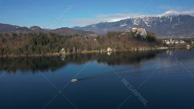 Electric boat sailing on calm Lake Bled under the castle aerial