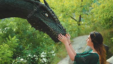 Fantasy portrait woman queen, hand touches muzzle of ancient dragon. Green vintage silk dress golden crown, fabric fly