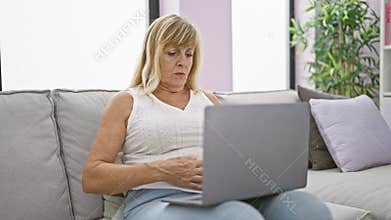Aching tummy turns blonde, middle age woman\'s sofa-sitting laptop use into grueling ordeal at home