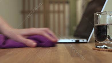 Hand with cloth cleaning workplace, wood work desk from dust on desktop surface. Wiping table with fiber
