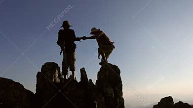 silhouette of People helping each other hike up a mountain at sunrise. Giving a helping hand, and active fit lifestyle concept.