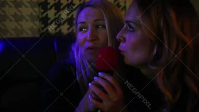 Two joyful women singing in a microphone at a