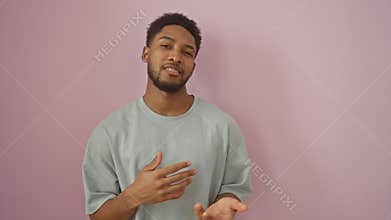 Clueless african american guy wearing a t-shirt, shrugging on an isolated pink background, shows puzzled face in doubt, a portrait