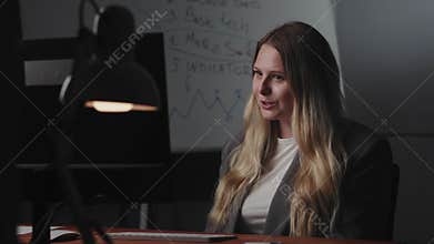 A young blonde girl blogger, entrepreneur or student sits at workplace at the table, uses a computer, looks at the