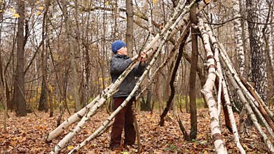 Boy builds hut frame from thin trunks and branches