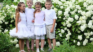 Two boys and two girls stand and smile near bush