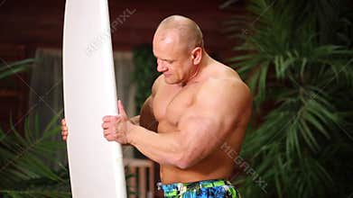 Muscular man stands against bungalow and examines