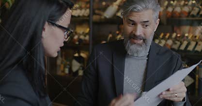 Mature businessman talking to female colleague discussing document doing high-five in restaurant