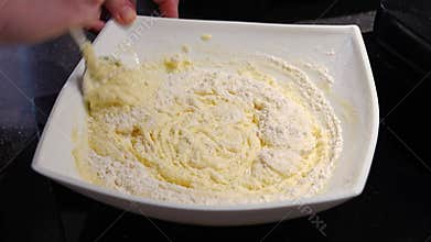 A woman&#x27;s hand mixes the dough with the added flour with a spoon.