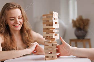 two women playing Jenga board game at home, excitement and relaxation, mind development concept,