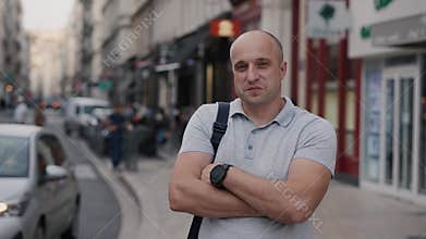Confident man poses on city street with modern architecture and busy pedestrians
