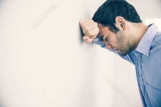 Depressed man leaning his head against a wall
