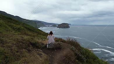 View from the back, woman sitting on a rock on a rock above the sea