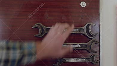 A hand is adjusting wrenches on a wooden door using mechanics tools in a garage