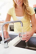 Woman Pouring Glass Of Water From Tap In Kitchen