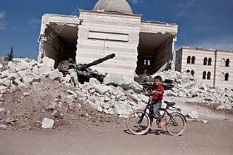 A syrian boy on bike outside of the damaged mosque in Azaz, Syria.