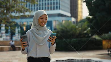 Cute Islamic Lady Going on the Street, Texting in Smartphone Holding Coffee.