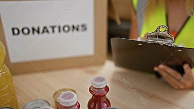 Blonde woman organizing donations in a warehouse with clipboard, beverages, and canned food in focus