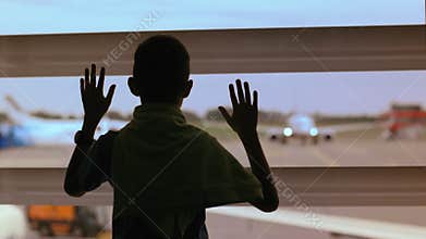 Aspiring Pilot: Boy Watches Airplanes at Airport Window