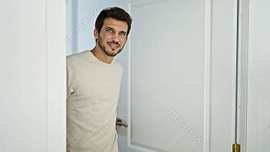 Smiling young man with a beard opening a white door inside a bright home