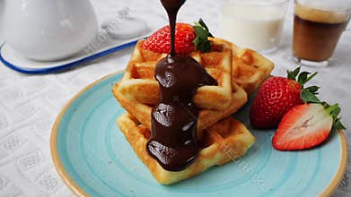 Liquid dark chocolate sauce is poured on belgian waffles. Sweet breakfast strawberry coffee milk.