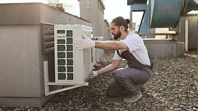 Worker crouching and holding hand on conditioner outdoor