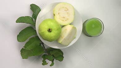 Top view rotation of a whole and half fresh ripe guava in white ceramic plate.