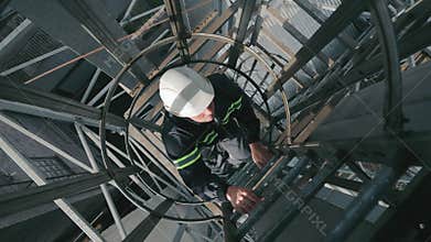 Industrial Worker Climbing Ladders Up. Top view, Worker with hard hat ascending the ladder in an industrial environment.