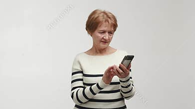 An elderly focused woman adjusts finger, holds in hands and uses a smartphone to type and respond to messages. An aged