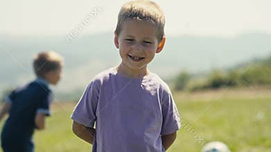 Boy Smiles With Caries on His Teeth As Another Boy Chases A Ball Behind Him