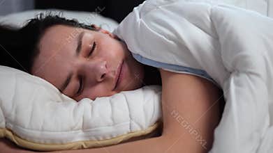 In the quiet of dawn, young brunette woman lies amidst soft white pillows, her eyes opening slowly to the day. This