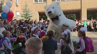 Knowledge day. September 1st. A festive school lineup. A white teddy bear animator dances with first graders