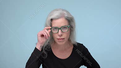 A woman with stunning gray hair looks over her green-rimmed glasses with a critical or questioning expression.